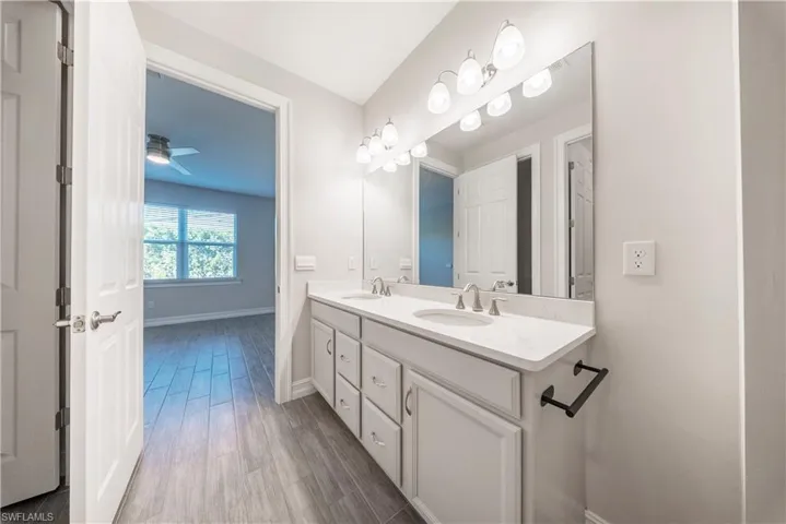 Full bathroom with double vanity, dark wood-style flooring, and a ceiling fan