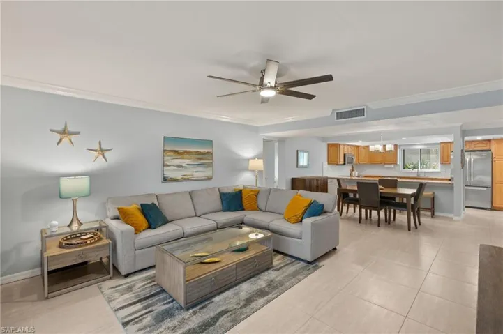 Living area featuring light tile patterned floors, visible vents, ornamental molding, and ceiling fan with notable chandelier