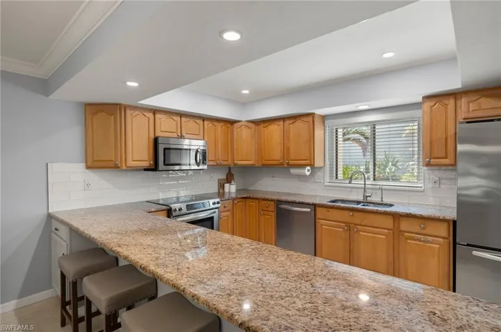 Kitchen featuring appliances with stainless steel finishes, a breakfast bar, light stone counters, and a sink