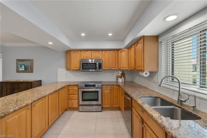 Kitchen featuring light stone countertops, recessed lighting, appliances with stainless steel finishes, backsplash, and a sink