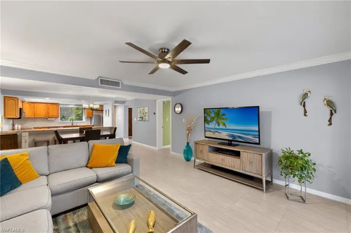 Living room with baseboards, visible vents, ceiling fan with notable chandelier, and crown molding