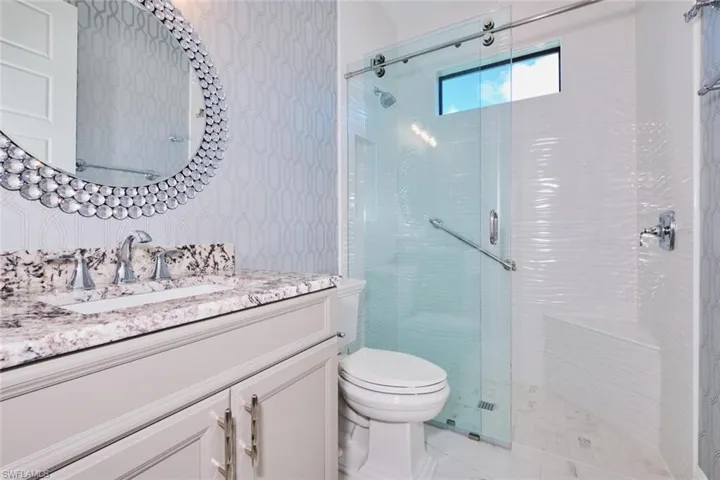 Full bathroom with wallpapered walls, vanity, and a stall shower