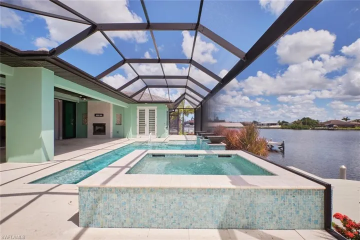 Swimming pool with an in-ground hot tub, a water view, a patio area, ceiling fan, and glass enclosure