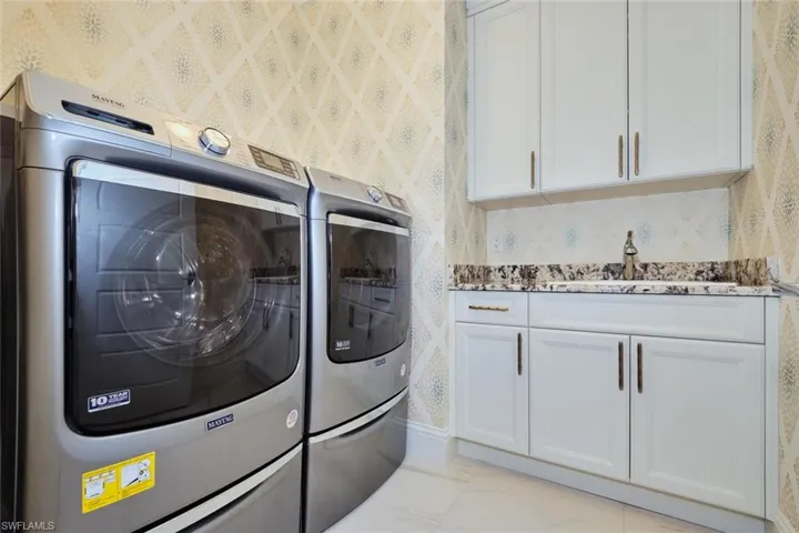 Washroom featuring wallpapered walls, washing machine and clothes dryer, cabinet space, and light marble finish flooring
