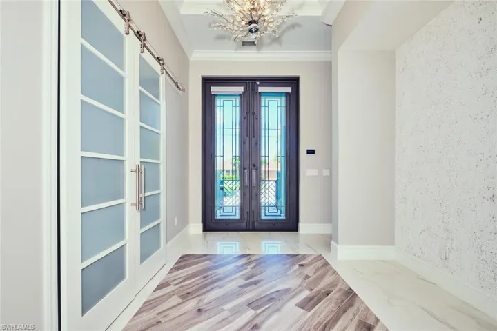 Foyer entrance with french doors, a chandelier, ornamental molding, a barn door, and marble finish floors