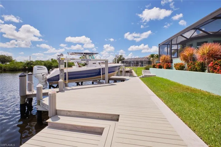 Dock featuring boat lift, a water view, glass enclosure, and a yard