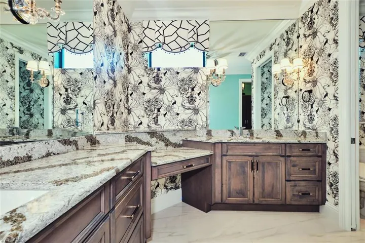Bathroom with ornamental molding, two vanities, a chandelier, and marble finish floors