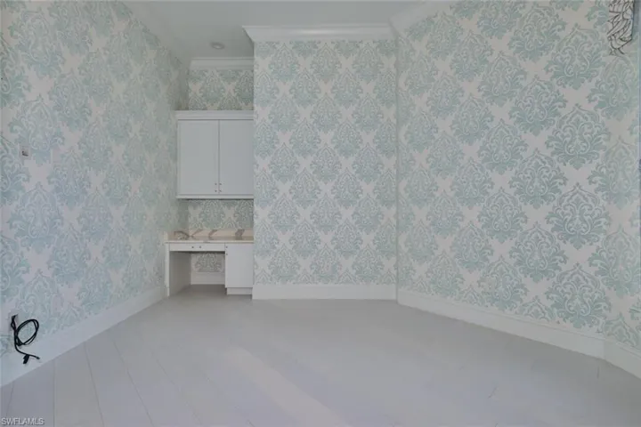 Unfurnished room featuring crown molding, wallpapered walls, built in study area, and light wood finished floors