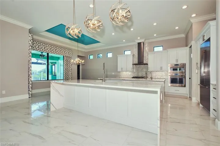 Kitchen featuring a chandelier, stainless steel appliances, wall chimney range hood, light marble finish floors, and plenty of natural light