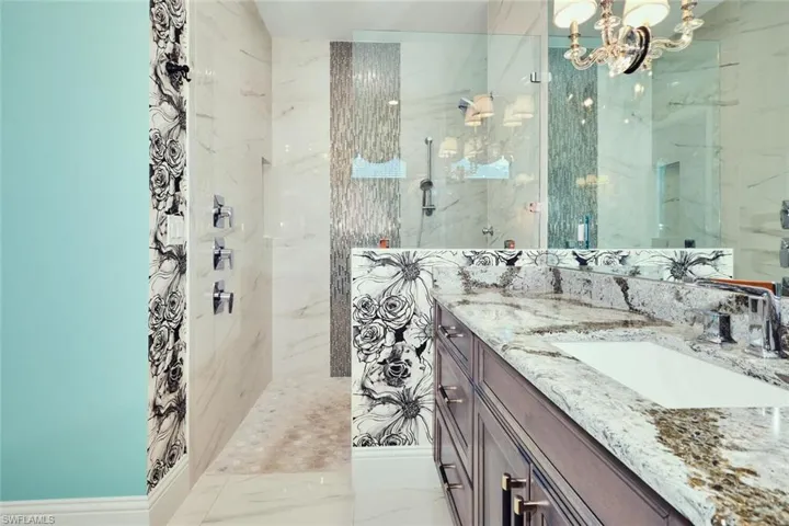 Bathroom featuring vanity, a marble finish shower, marble tiled floors, and a chandelier