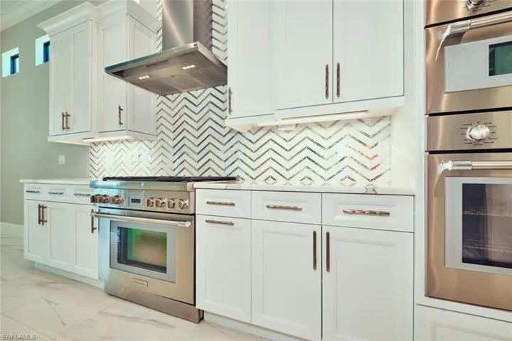 Kitchen with wall chimney range hood, appliances with stainless steel finishes, light marble finish flooring, decorative backsplash, and white cabinets