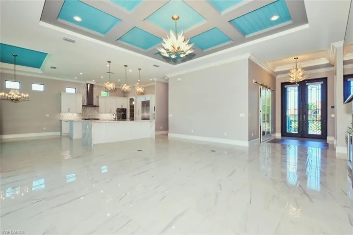 Unfurnished living room with a chandelier, plenty of natural light, crown molding, coffered ceiling, and light marble finish floors