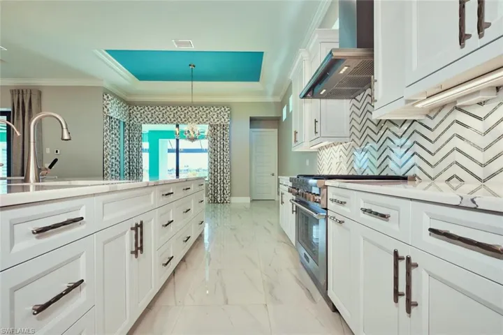Kitchen featuring custom range hood, high end stainless steel range, crown molding, a raised ceiling, and light countertops