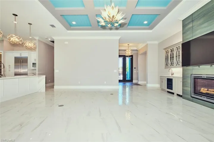 Unfurnished living room with a chandelier, crown molding, wine cooler, coffered ceiling, and a fireplace