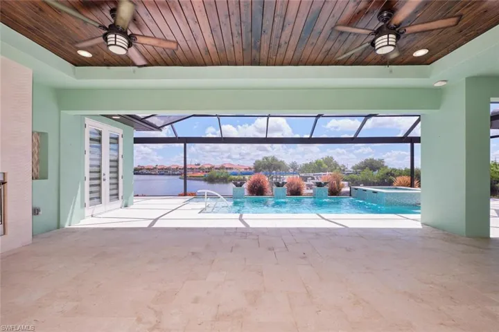 View of swimming pool with a ceiling fan, a water view, french doors, and a pool with connected hot tub