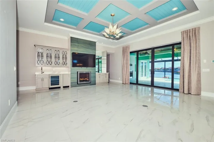 Unfurnished living room featuring beverage cooler, healthy amount of natural light, ornamental molding, coffered ceiling, and light marble finish flooring