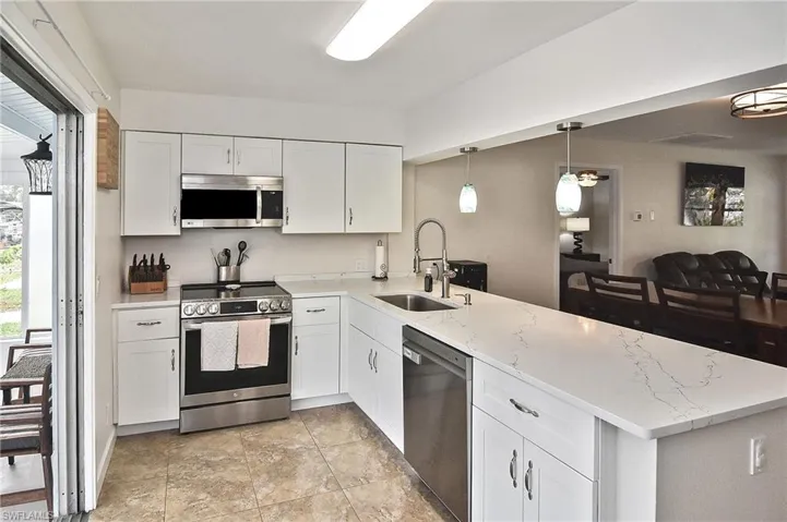 Kitchen featuring light stone countertops, a peninsula, white cabinetry, appliances with stainless steel finishes, and a sink