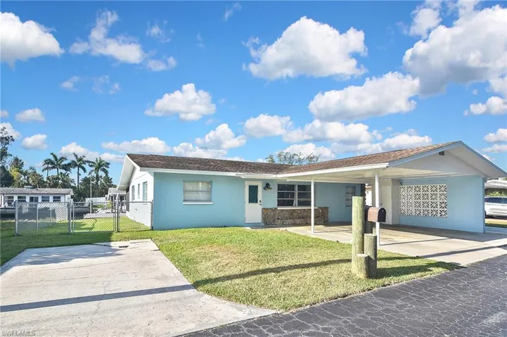 View of front of house with concrete driveway, stucco siding, an attached carport, a front yard, and a gate