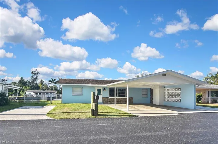 View of front facade featuring a front lawn, fence, an attached carport, and stucco siding