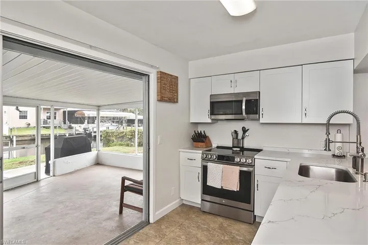 Kitchen with appliances with stainless steel finishes, a sink, white cabinetry, and light stone counters