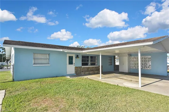 Rear view of house featuring a yard, stucco siding, fence, and an attached carport