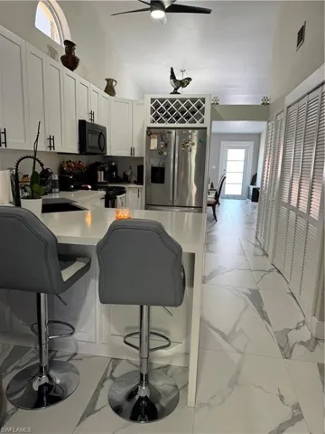 Kitchen featuring light tile patterned flooring, white cabinetry, a kitchen breakfast bar, ceiling fan, and stainless steel fridge