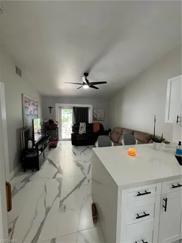 Kitchen featuring light tile patterned flooring, ceiling fan, white cabinets, light stone countertops, and lofted ceiling