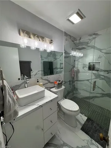 Bathroom featuring a shower with shower door, tile walls, toilet, tile patterned floors, and vanity