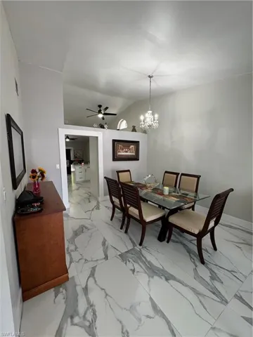 Tiled dining room with ceiling fan with notable chandelier and lofted ceiling