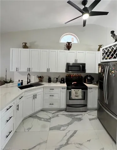 Kitchen featuring white cabinetry, stainless steel appliances, lofted ceiling, and sink