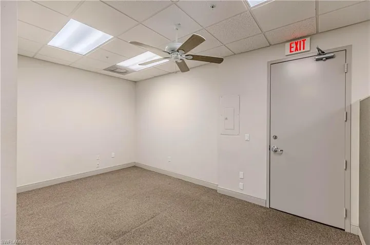 Carpeted empty room featuring a paneled ceiling, ceiling fan, and electric panel