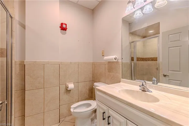 Bathroom featuring a shower with door, toilet, and tile walls