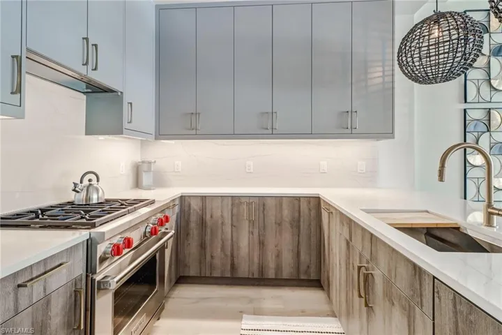 Kitchen featuring premium range, under cabinet range hood, light stone countertops, light wood-style flooring, and tasteful backsplash