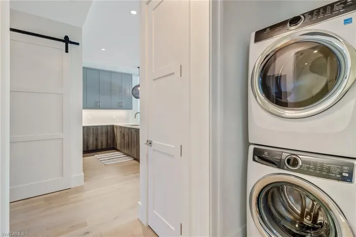 Washroom with a barn door, light wood-style floors, estacked washer and dryer, and recessed lighting