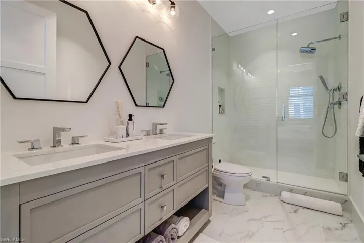 Bathroom featuring a stall shower, double vanity, light marble finish flooring, and recessed lighting