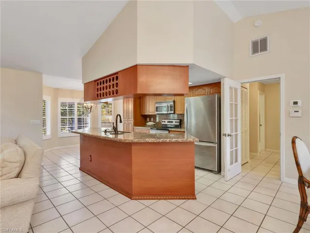 Kitchen featuring appliances with stainless steel finishes, light stone counters, light tile patterned floors, high vaulted ceiling, and open floor plan