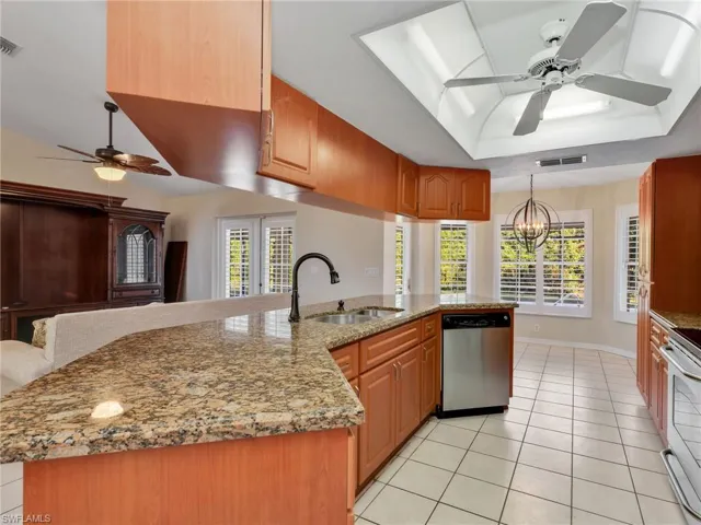 Kitchen with a ceiling fan, light stone counters, light tile patterned floors, and brown cabinets