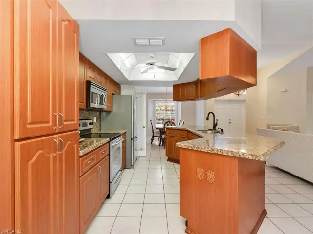 Kitchen featuring appliances with stainless steel finishes, a raised ceiling, dark stone countertops, and a peninsula