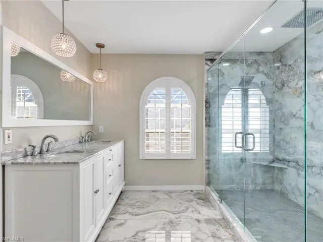 Bathroom featuring double vanity, light marble finish flooring, healthy amount of natural light, and a marble finish shower