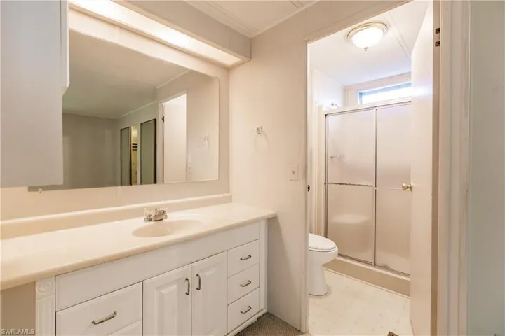 Bathroom featuring vanity with extensive cabinet space, tile flooring, toilet, and a shower with door