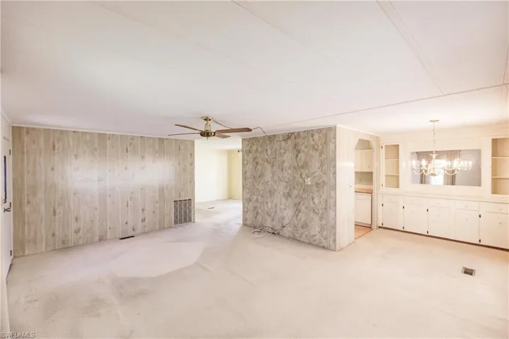 Empty room with light colored carpet, built in shelves, and ceiling fan with notable chandelier