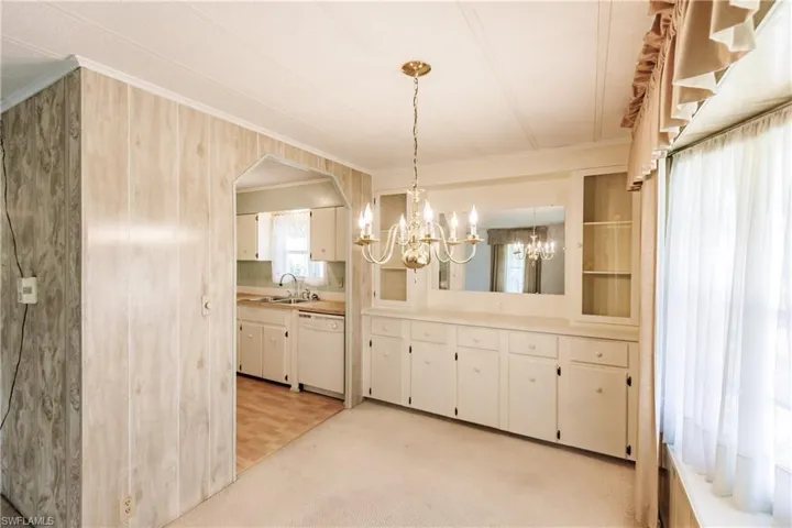 Unfurnished dining area with a notable chandelier, sink, ornamental molding, and light colored carpet