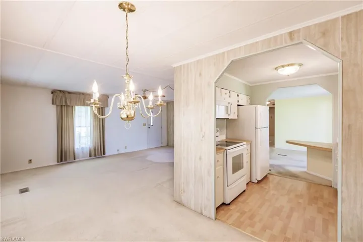 Kitchen with decorative light fixtures, white cabinetry, ornamental molding, light carpet, and white appliances