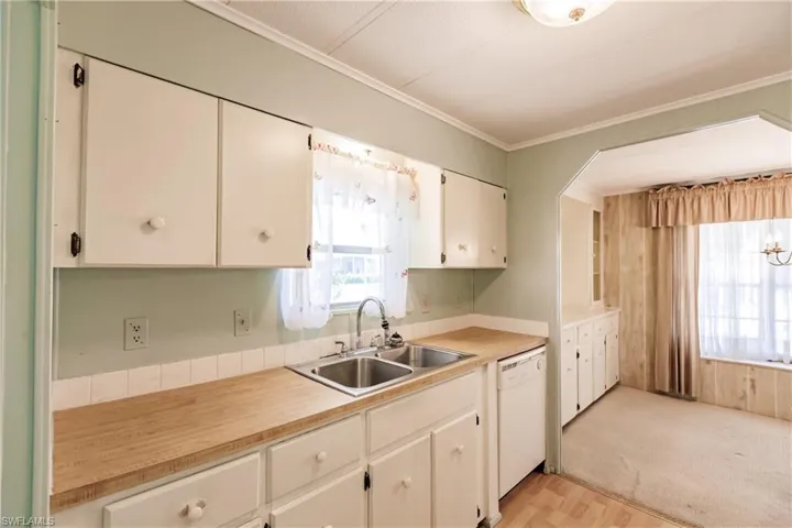 Kitchen featuring dishwasher, white cabinetry, ornamental molding, light colored carpet, and sink
