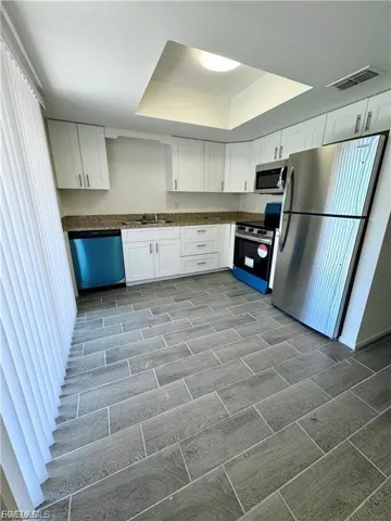 White cabinetry, stainless steel appliances, granite countertops, tile flooring, and a ceiling skylight