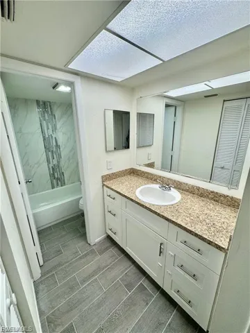 Bathroom featuring a white vanity with a speckled countertop, a large wall-mounted mirror, and plank-style floor tiling