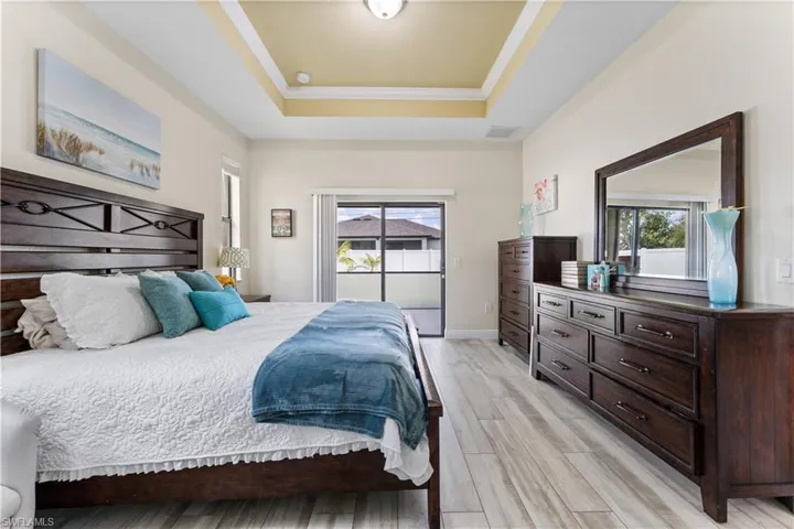 Bedroom with a raised ceiling, light wood finished floors, baseboards, and multiple windows