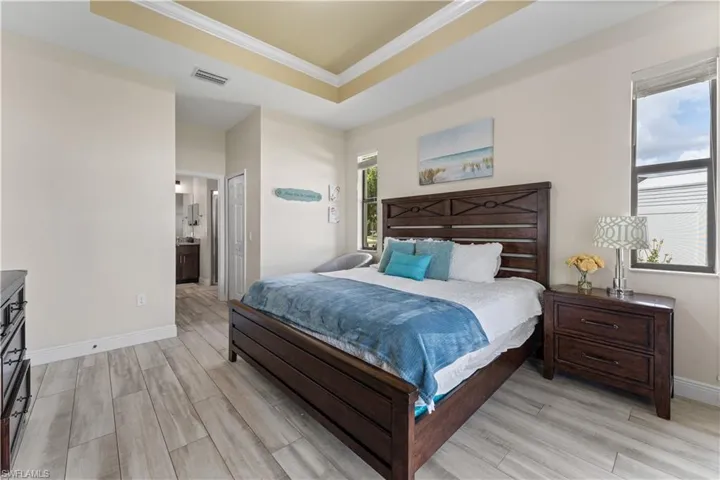 Bedroom featuring crown molding, visible vents, a raised ceiling, light wood finished floors, and baseboards