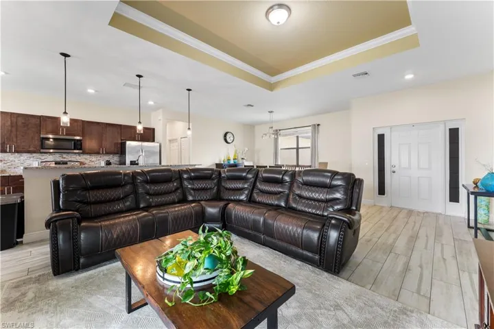 Living area with ornamental molding, visible vents, wood tiled floor, a raised ceiling, and baseboards