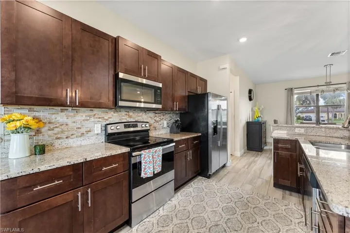 Kitchen featuring light stone countertops, visible vents, appliances with stainless steel finishes, a sink, and decorative backsplash